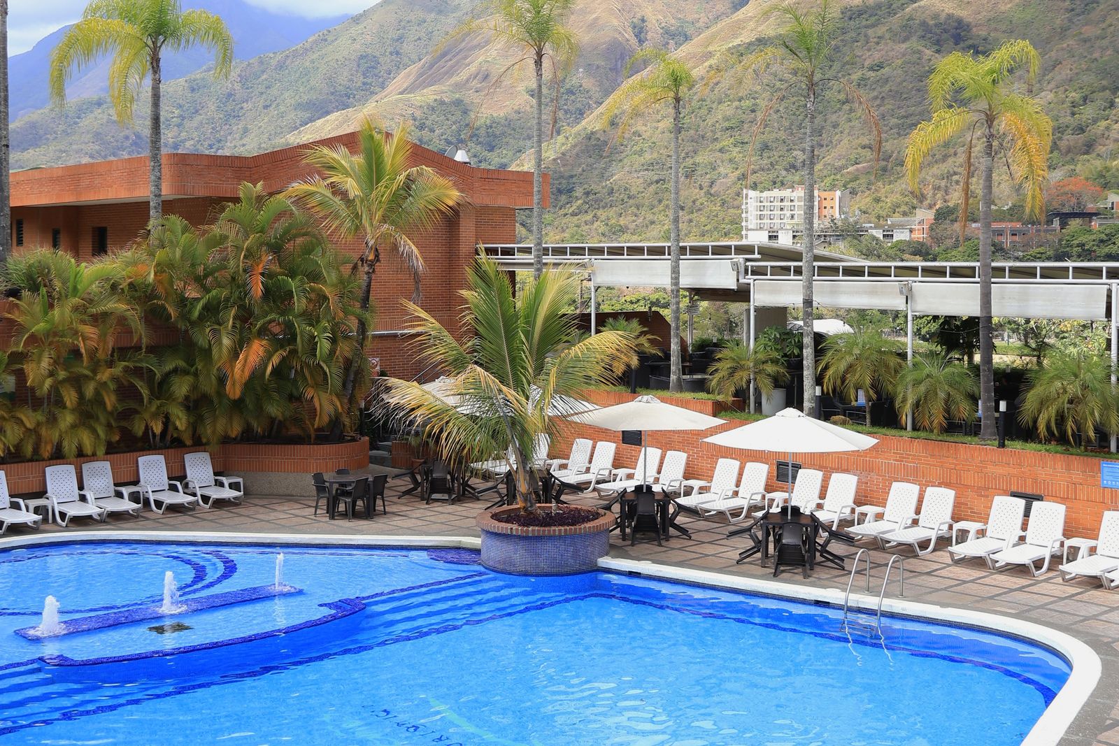 Piscina del hotel con palmeras y el cerro El Ávila al fondo
