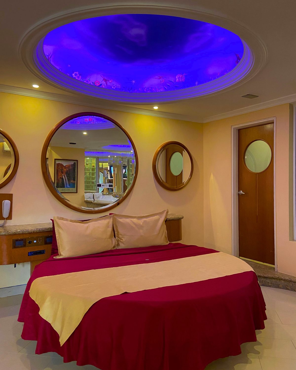Paradise: cama redonda bajo una cúpula iluminada en morado, con espejos redondos