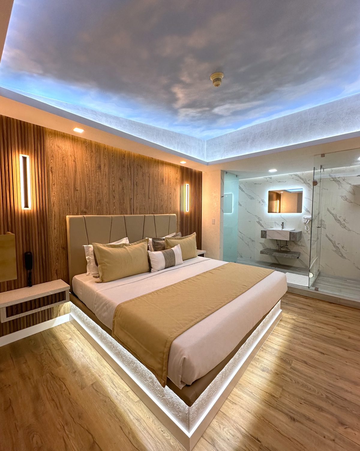 Ávila: cama con luz en la base, techo de cielo con nubes y el baño al fondo