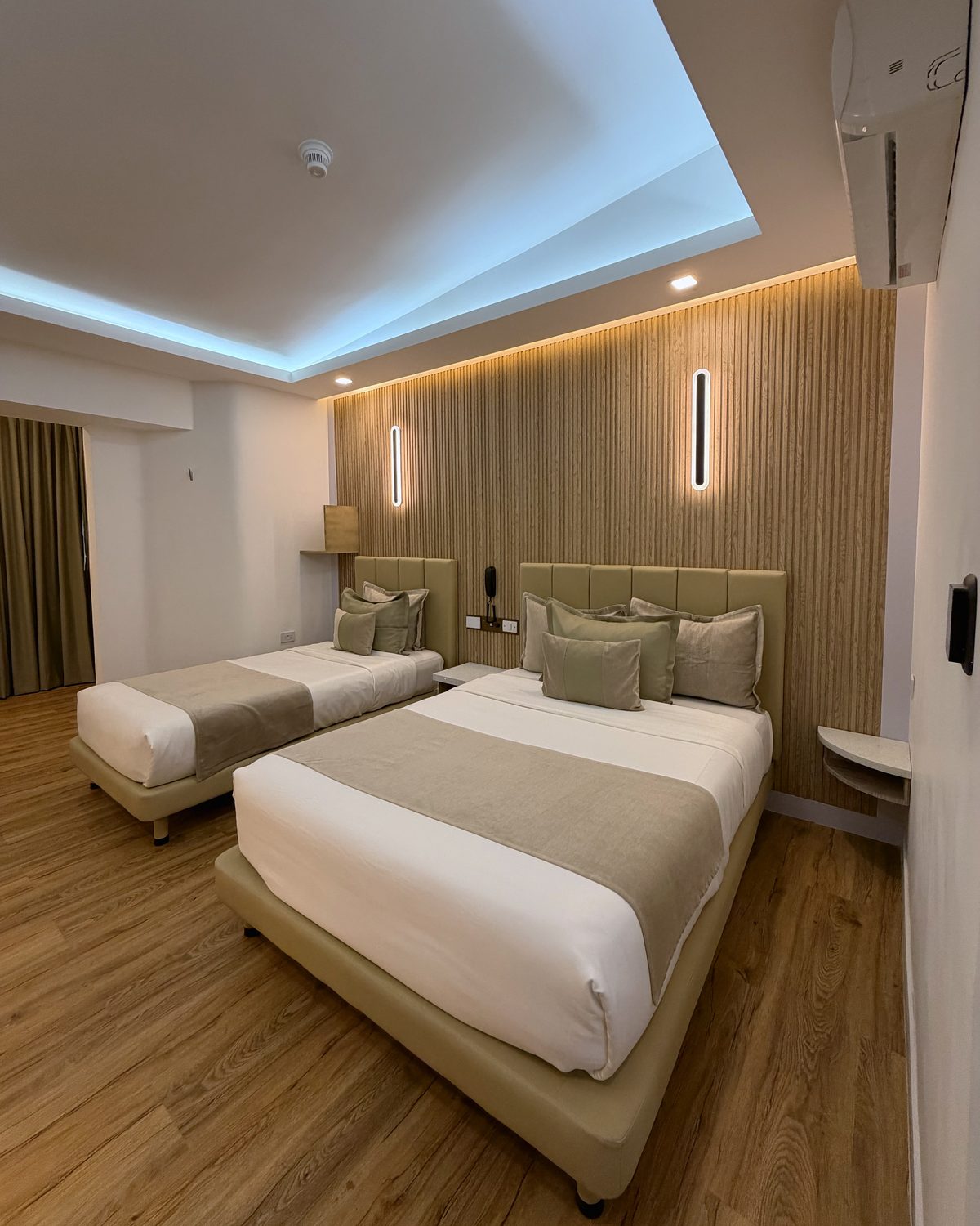 Doble Remodelada con una cama matrimonial y una individual, pared de listones de madera y luz indirecta