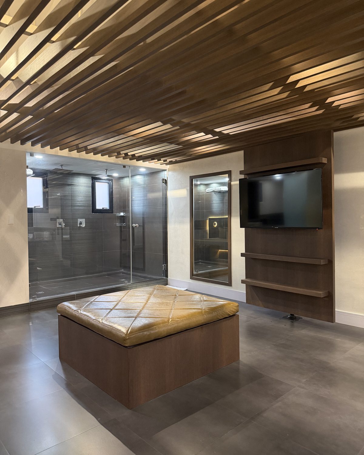 Seven: puf de cuero, ducha de vidrio y televisor en panel de madera