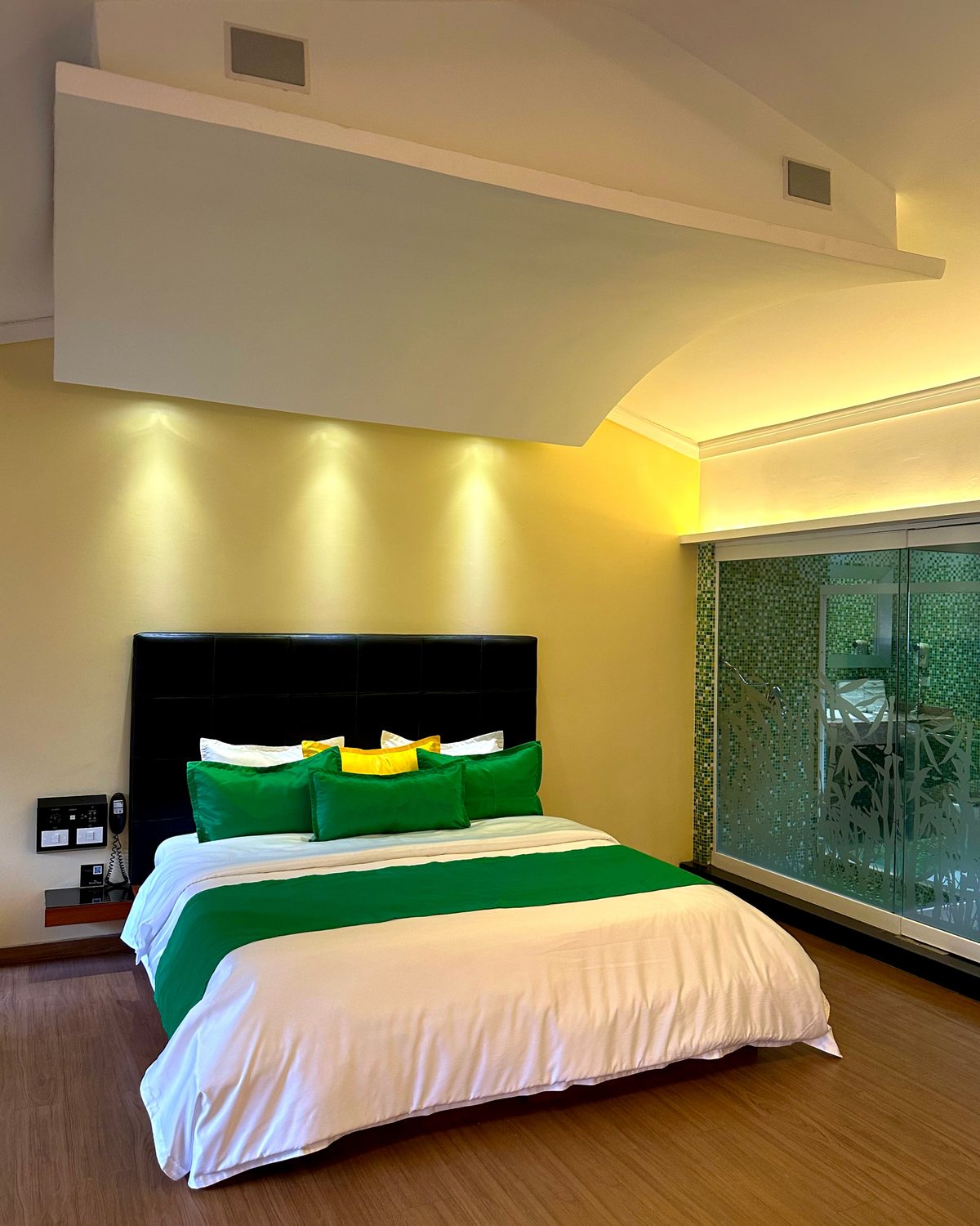 Zen Premium: cama con cojines verdes, cabecero negro y techo con luz indirecta