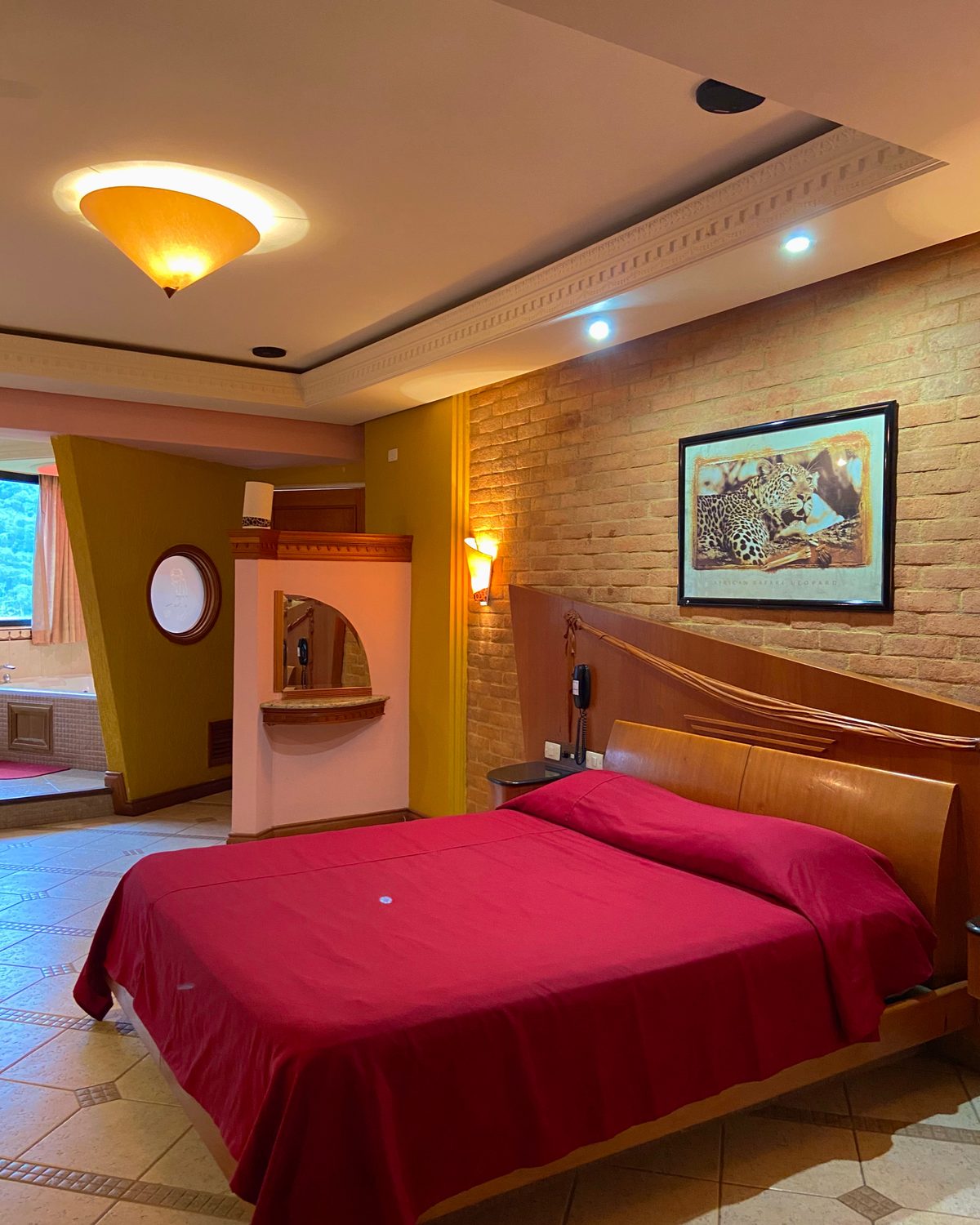 Temática Jacuzzi (Africana): cama matrimonial con cubrecama rojo, pared de ladrillo y cuadro de leopardos
